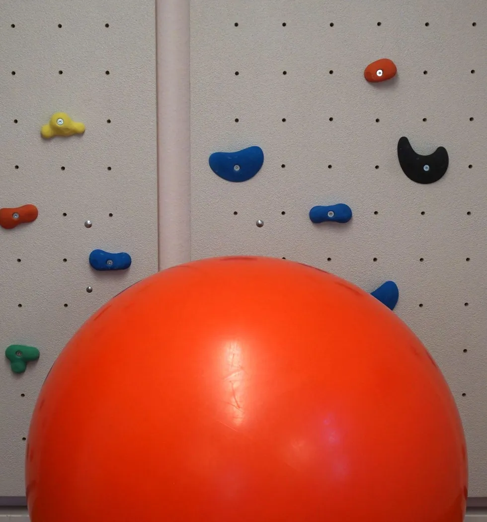 Therapeuthische Kletterwand. Davor ein großer roter Gymnastikball.